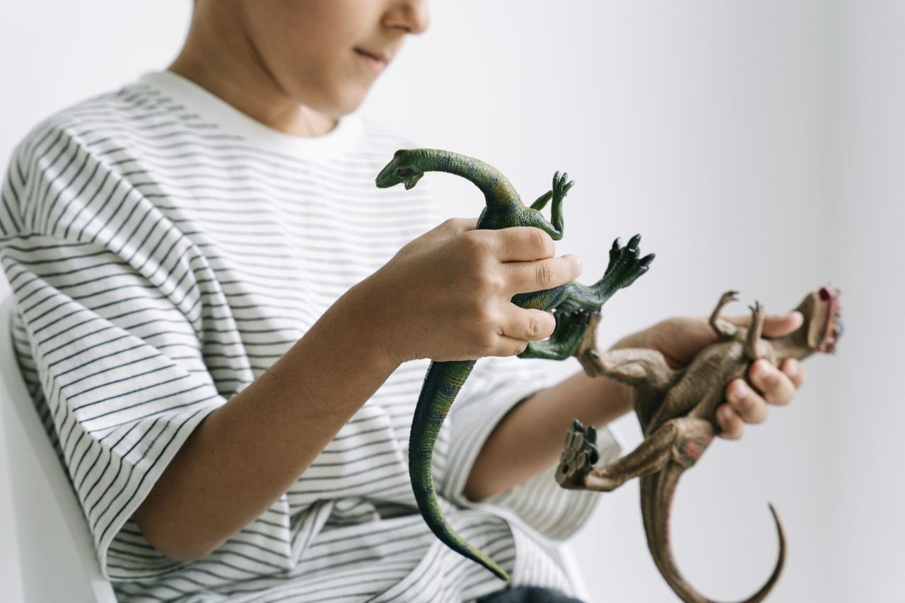A child in a striped shirt engaging with toy dinosaurs in a playful setting.