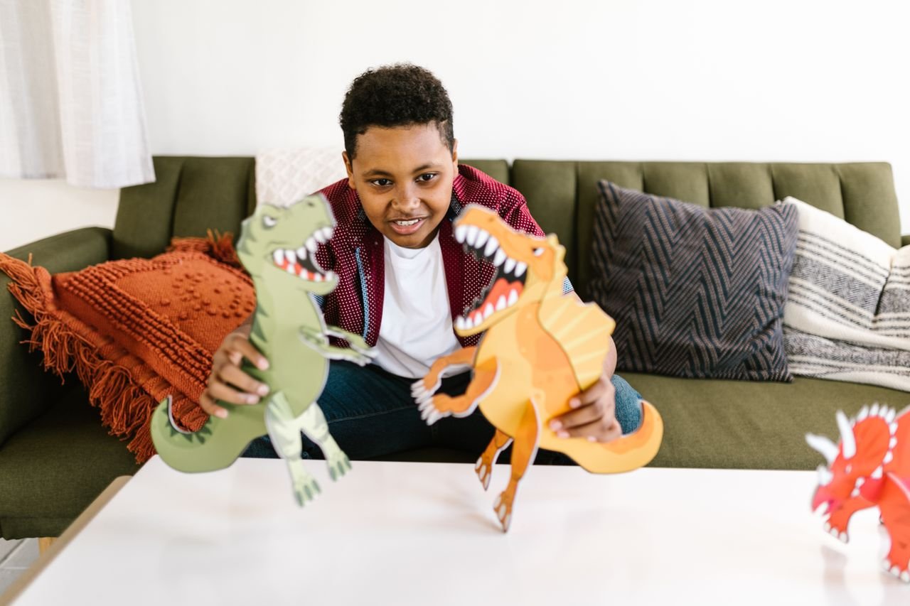 collection-03 Young boy sitting on couch playing with paper dinosaur cut-outs, fostering creativity and learning.