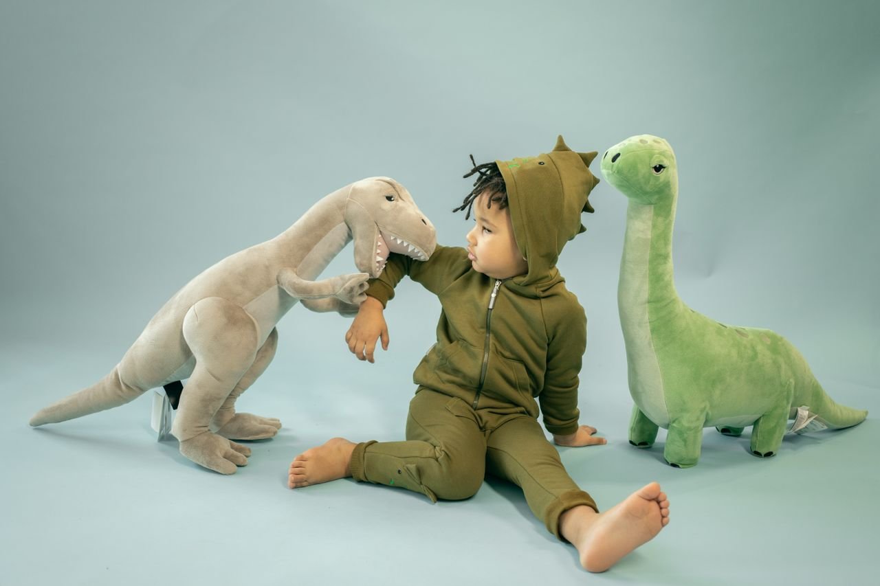 summer-sale African American child with dreadlocks in dinosaur costume sitting between soft toys representing bite concept