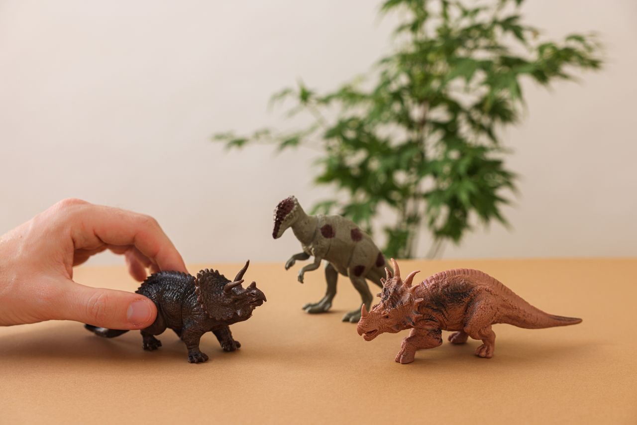 collection-01 Hand arranging dinosaur figurines on a brown surface with greenery background.
