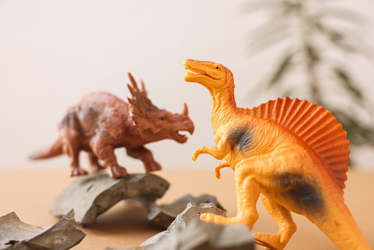 our-story-02 Close-up of dinosaur toys on a tabletop with broken shards, evoking prehistoric play.