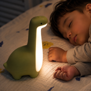 Veilleuse dinosaure verte près d’un petit garçon endormi.