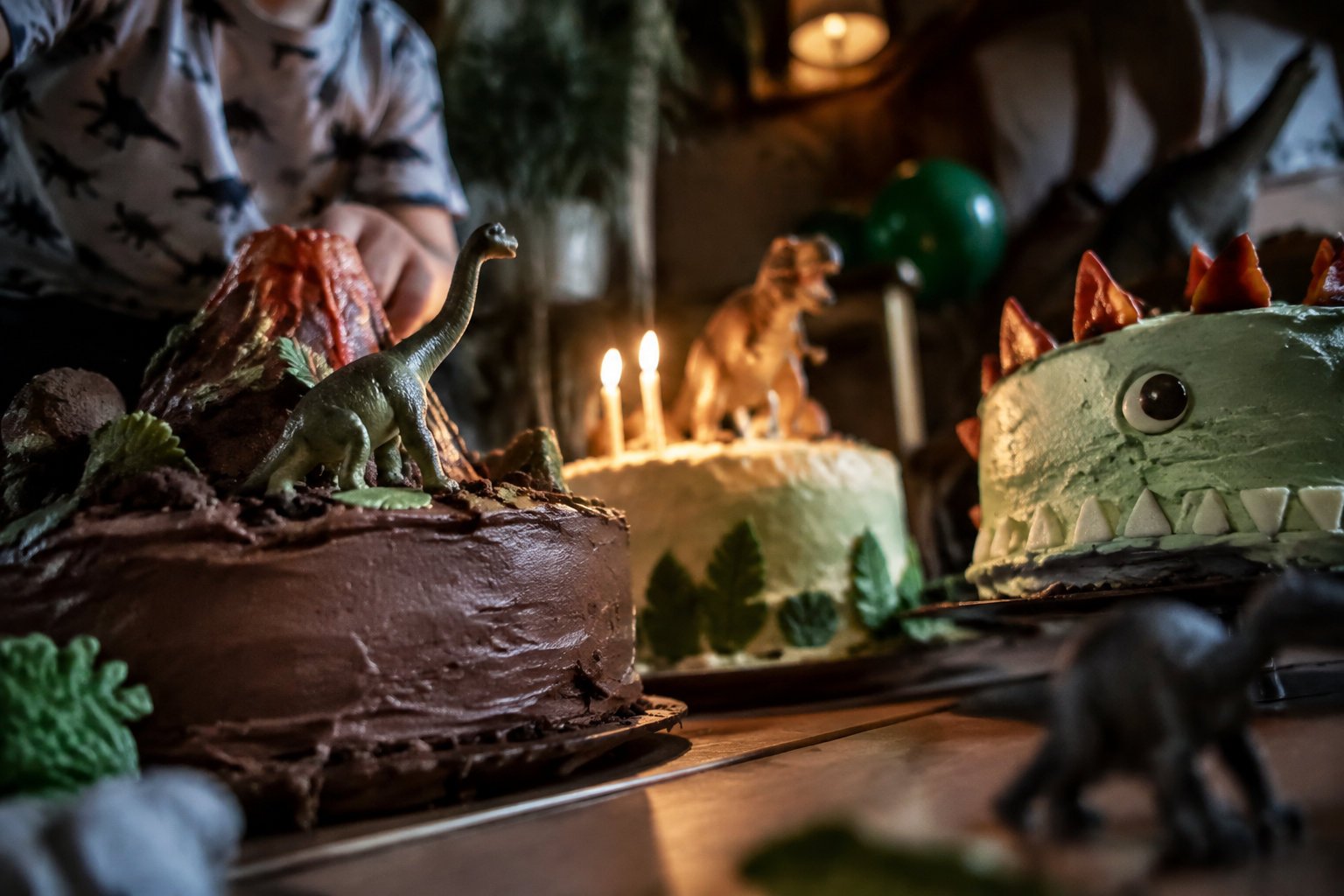 Trois gâteaux d'anniversaire sur le thème des dinosaures, décorés avec des figurines et un volcan en chocolat.